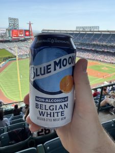 Hand holding a can of Blue Moon Non-Alcoholic beer with Angels Stadium baseball diamond in the background