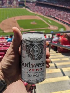 Hand holding a can of Bud Zero NA beer with Great American Ballpark field in the background